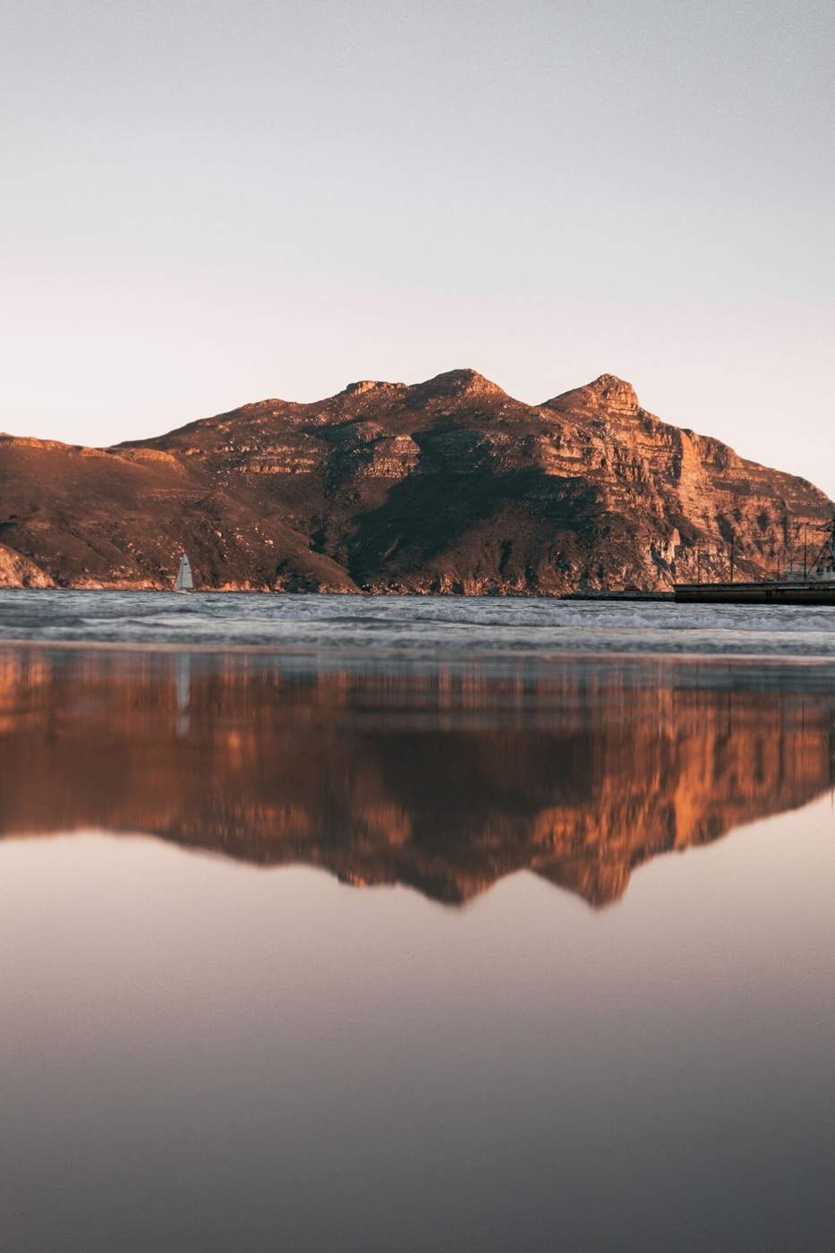 A red mountain mirrored in the wet sand of Hout Bay at dusk