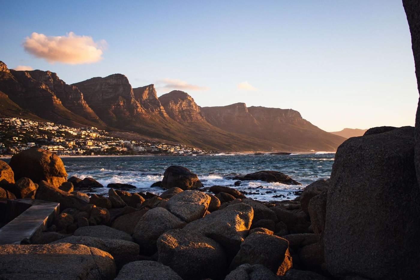 The Twelve Apostles glowing above Camps Bay at sunset, with boulders in the foreground