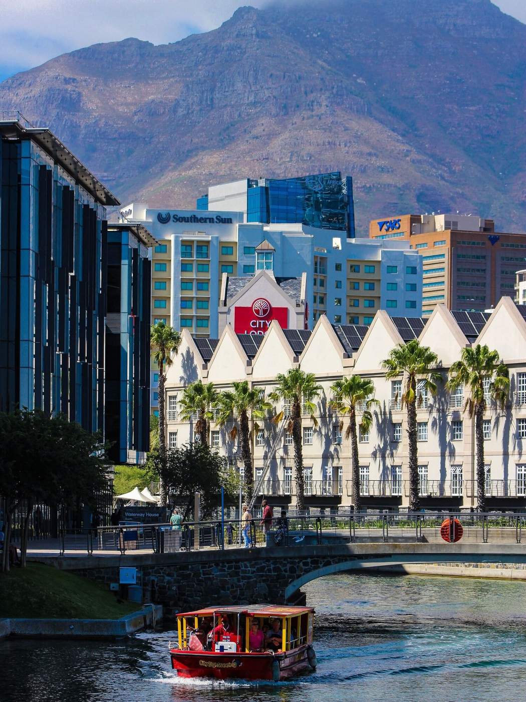 A red canal boat below palm trees and buildings at the V&A Waterfront, with Table Mountain behind